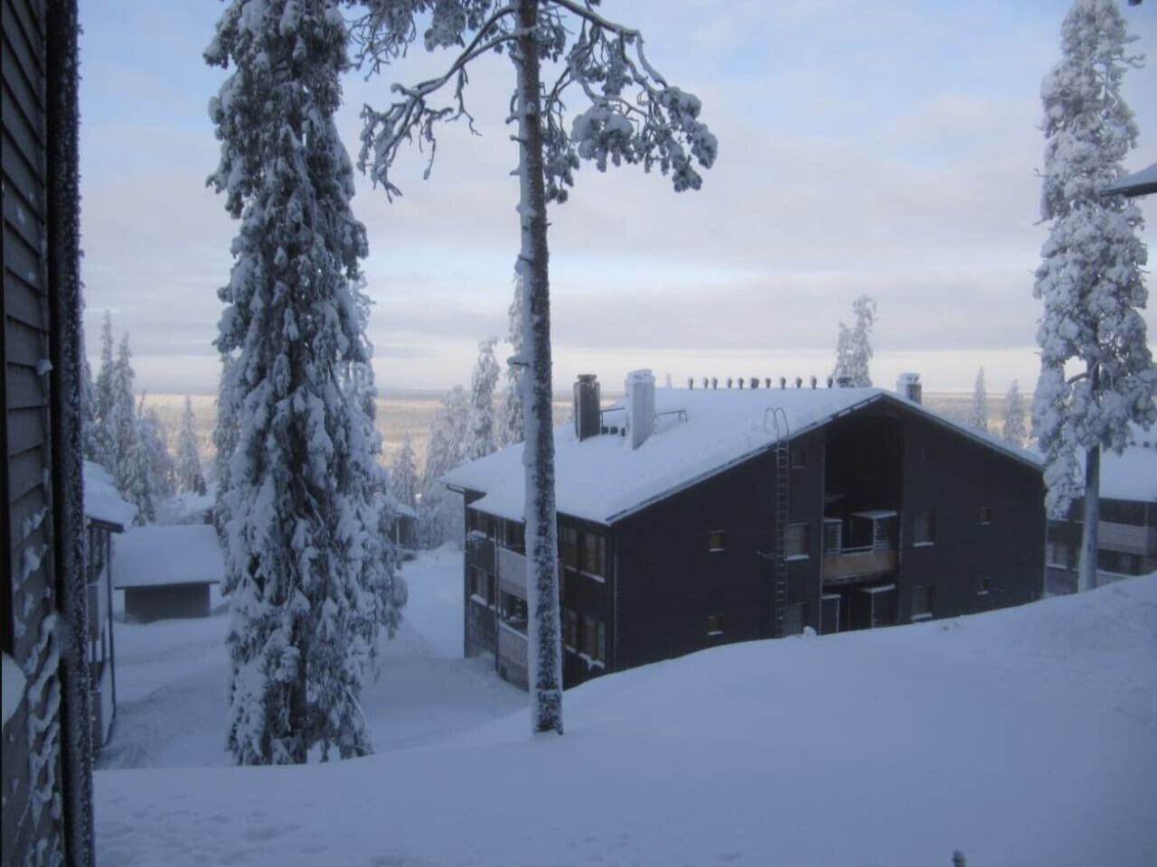 Ein schneebedecktes Gebäude mit Balkon, umgeben von schneebedeckten Bäumen.
