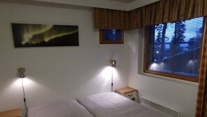 A room with a bed, two bedside lamps, a window with blinds, a radiator, and a wall-mounted picture. - Central 1BR Apt next to Ski Slopes | Ruka Centre (Ruka)