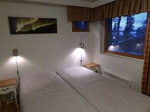 Ein Zimmer mit einem Bett, zwei Nachttischlampen, einem Fenster mit Jalousien, einem Heizkörper und einem Wandbild.