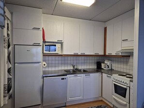 Eine kleine Küche mit weißen Schränken, einer Mikrowelle, einem Spülbecken, einem Herd und einem Geschirrspüler.