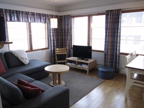 Ein Wohnzimmer mit einer Couch, einem kleinen runden Tisch, einem Fernseher auf einem Schrank und einem Esstisch mit Stühlen.