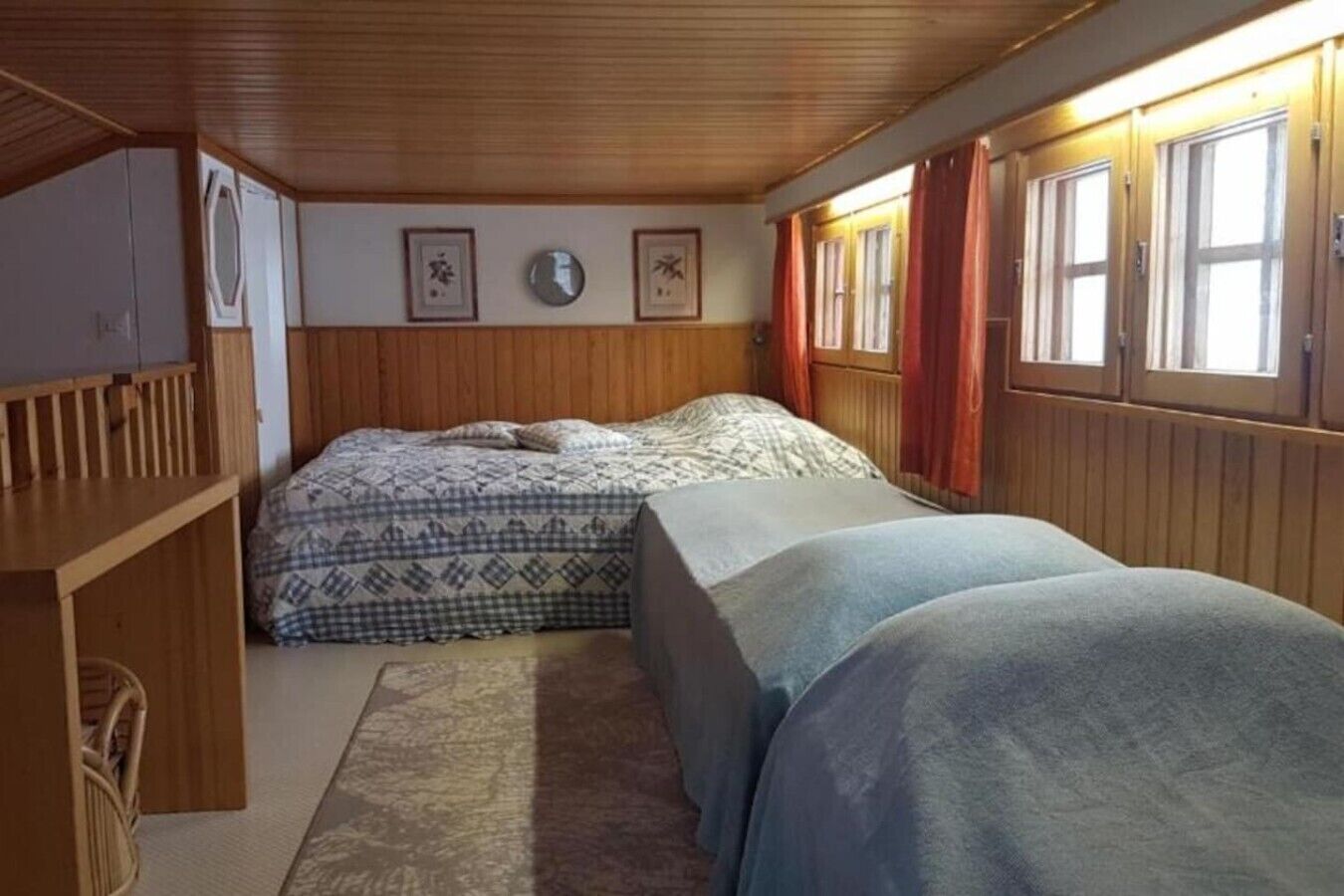 Una habitación con dos camas, paredes de madera, una mesita y una ventana con cortinas.