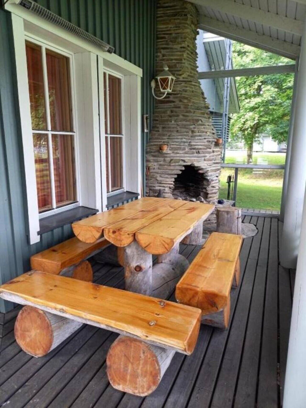 A wooden deck with a stone fireplace and a table with benches.