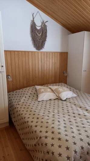 Ein Schlafzimmer mit einem hölzernen Kopfteil, einem Bett mit einem Bettbezug mit Sternenmuster und einem Wandbehang aus Makramee.
