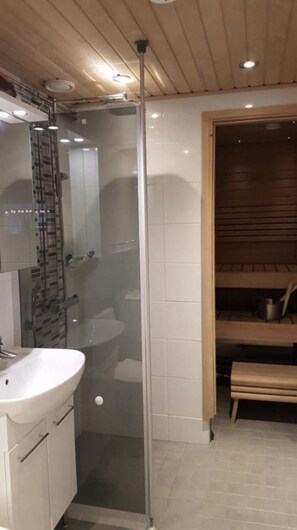 Ein Badezimmer mit Duschkabine aus Glas, einem Waschbecken und einer hölzernen Sitzbank.