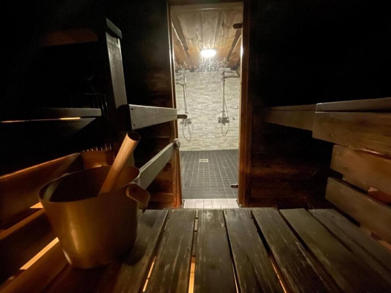 Saunassa on puiset lauteet, metallinen ämpäri ja laatoitettu lattia.