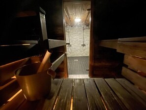 A sauna room with wooden benches, a metal bucket, and a tiled floor.