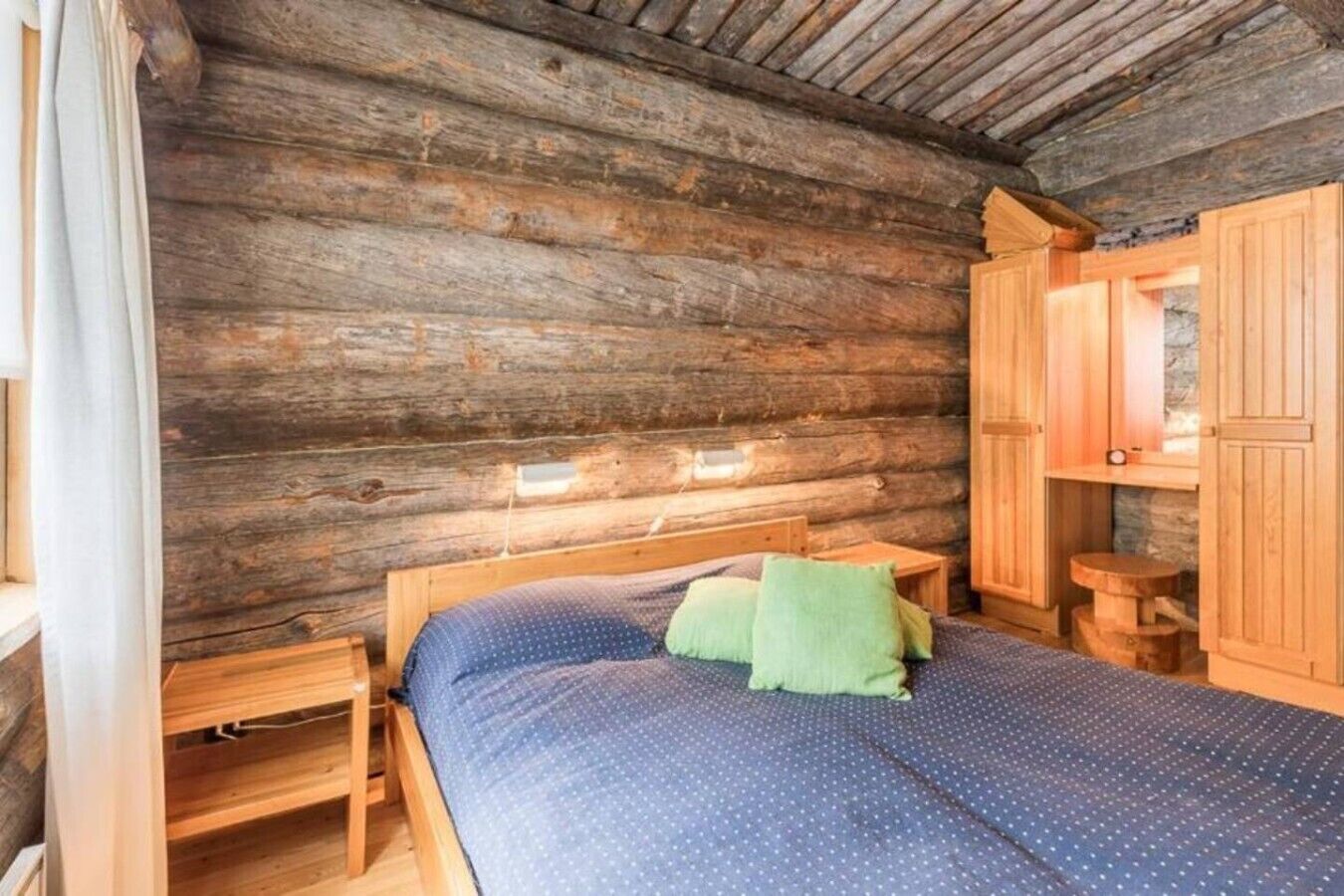 Una habitación tipo cabaña de madera con una cama, mesitas de noche de madera y una pequeña mesa.
