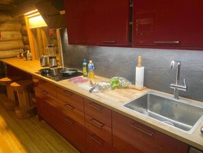 A kitchen with a wooden countertop, stainless steel sink, and red cabinets. - RukanTykky | Charming 3BR Chalet | Near Slopes (Ruka)