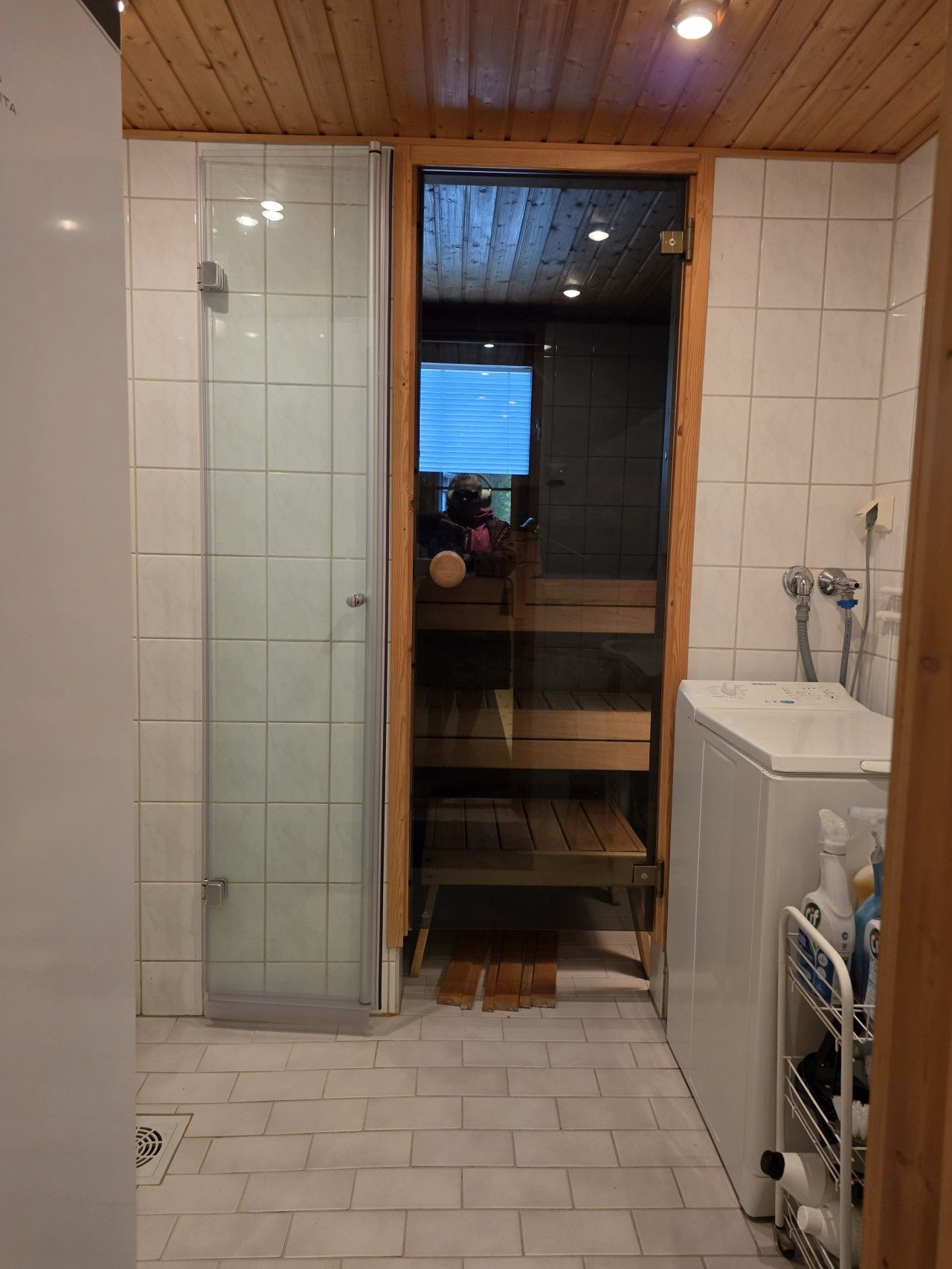 Un baño pequeño con cabina de ducha de vidrio, repisa de madera y lavadora.