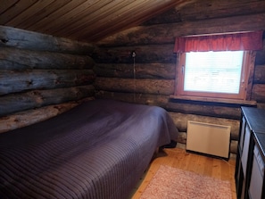 Ein Schlafzimmer in einer Blockhütte mit einem Bett, einem Fenster mit Jalousien, einem Heizkörper und einem Schminktisch.