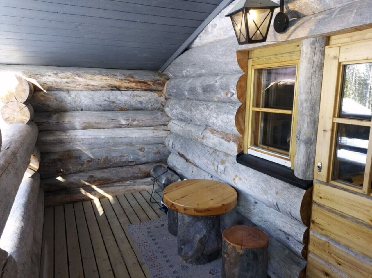 L’intérieur d’une cabane en rondins, avec un banc en bois, une petite table et une fenêtre donnant sur un paysage.