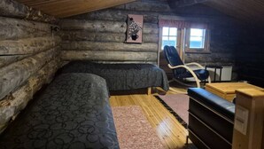 Habitación tipo cabaña de madera con dos camas, una mecedora y una pequeña mesa.