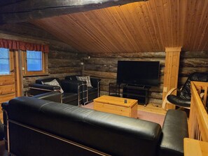 Ein Interieur einer Blockhütte mit einem schwarzen Ledersofa, einem Holztisch, einem Fernseher und einem Kamin.