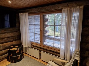 Ein Blockhaus-Zimmer mit großem Fenster, Heizkörper, gepolstertem Hocker und einem Gewebesessel.
