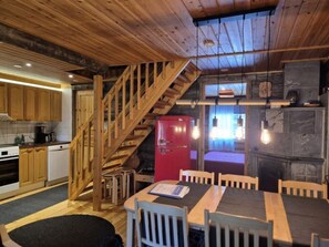 Une cuisine rustique avec des meubles de rangement en bois, un réfrigérateur rouge, un escalier en bois et un coin repas comprenant une table et des chaises.