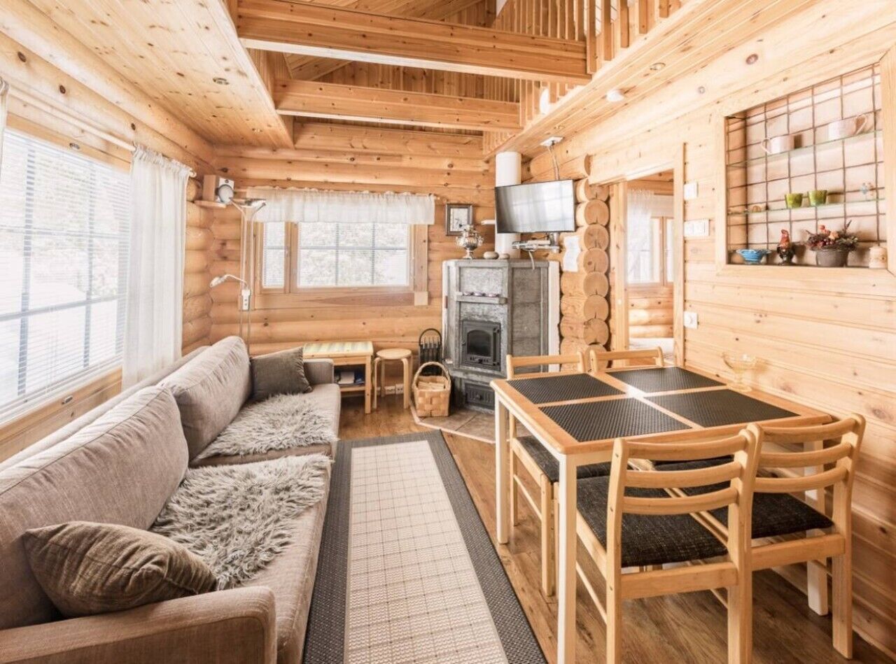 A log cabin interior with a sofa, dining table, chairs, a fireplace, and a television.