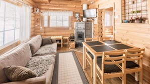 A log cabin interior with a sofa, dining table, chairs, a fireplace, and a television. - Mäntyruka A1 | Cozy 1BR Cabin with Loft & Sauna (Ruka)