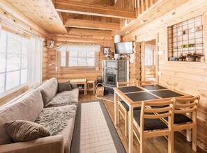 Ein rustikales Blockhaus-Interieur mit einer Couch, einem Esstisch, Stühlen, einem Kamin und einem Fernseher.