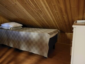 Ein kleines Zimmer mit einem Einzelbett, einer karierten Bettdecke, einer Holzbalkendecke und einem weißen Schrank.