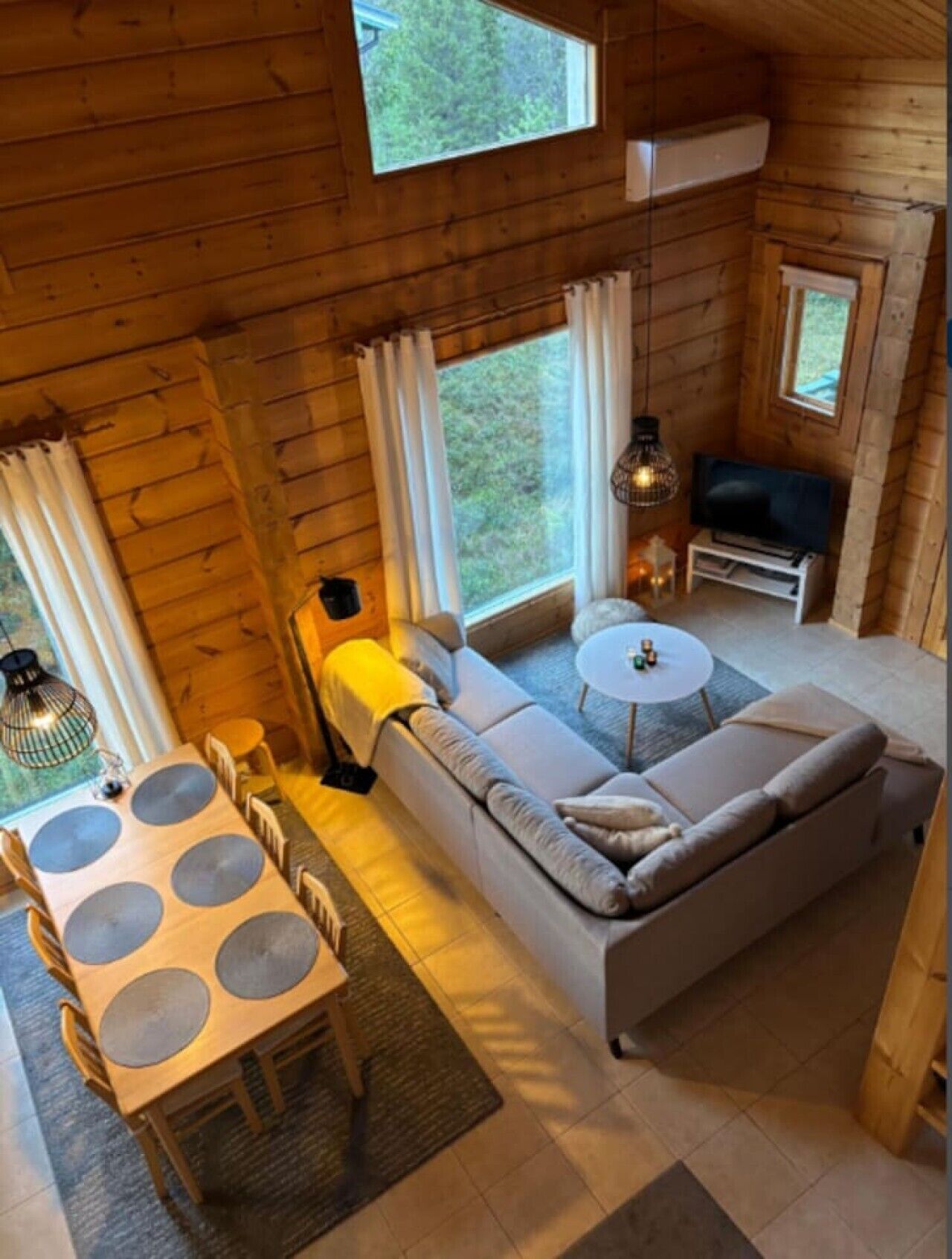 A cozy cabin interior with a sofa, dining table, and a television.