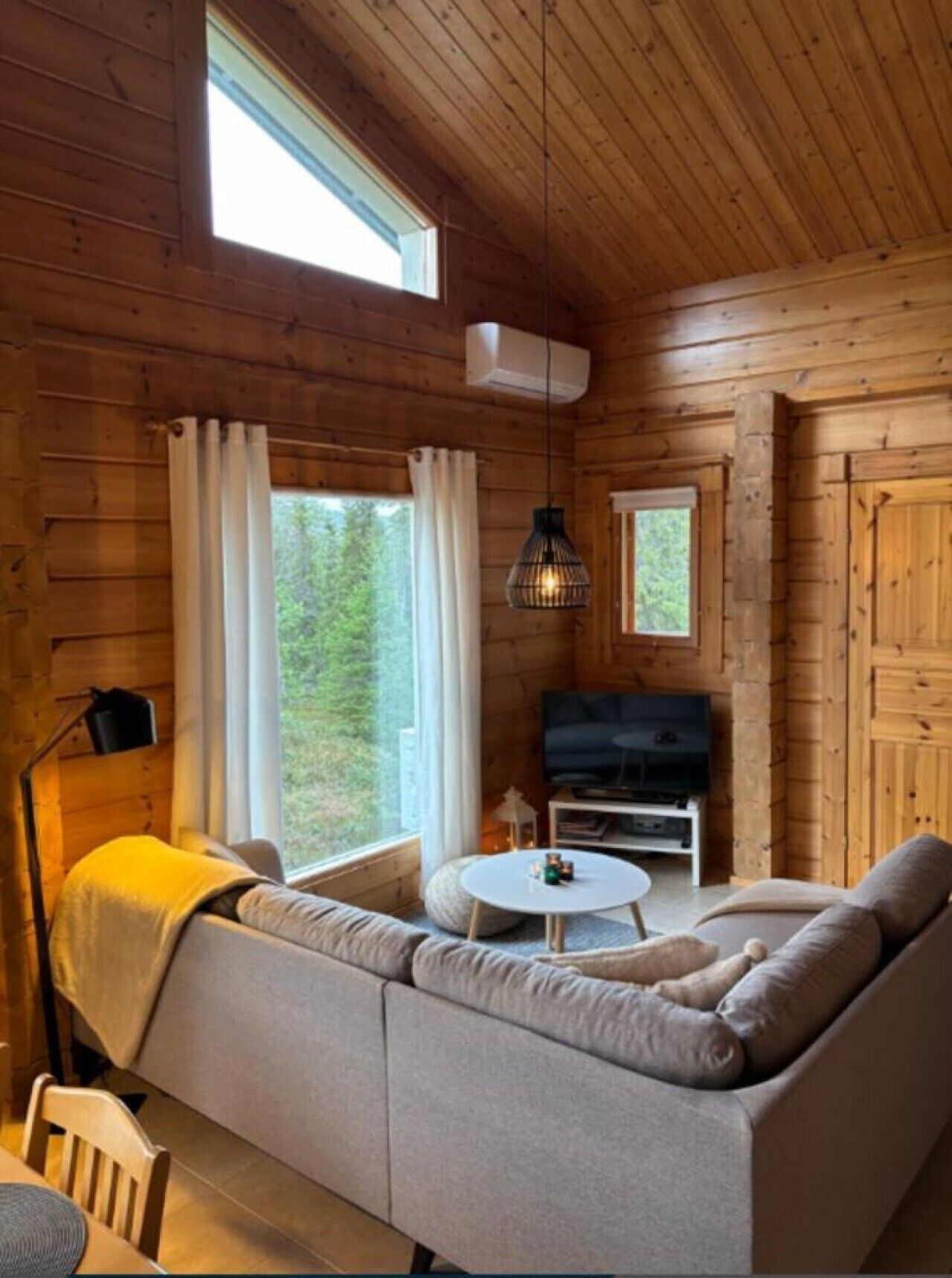A cozy cabin interior with a sofa, a round table, a television, and a window with curtains.