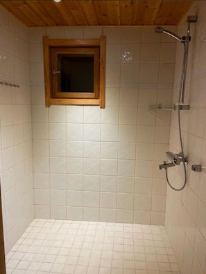Ein kleines Duschbad mit Fliesen und Holzboden, ausgestattet mit einem Fenster.