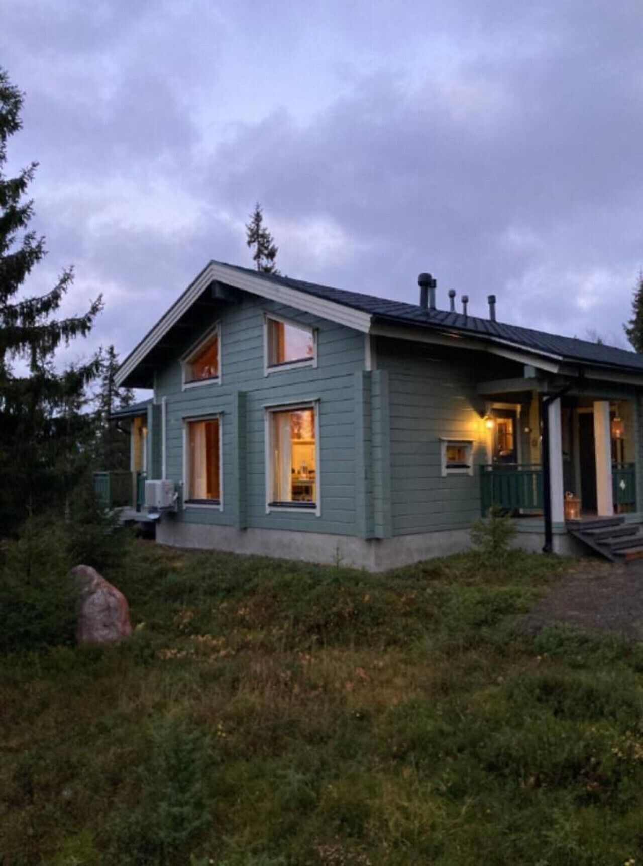 Kaksikerroksinen talo, jossa on kuisti, suuret ikkunat ja savupiippu.