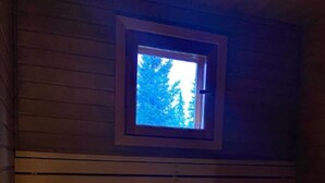 A sauna room with a bench, a small window, and a metal container. - Nietos A | Comfy Cabin in Ruka | Private Sauna (Ruka)