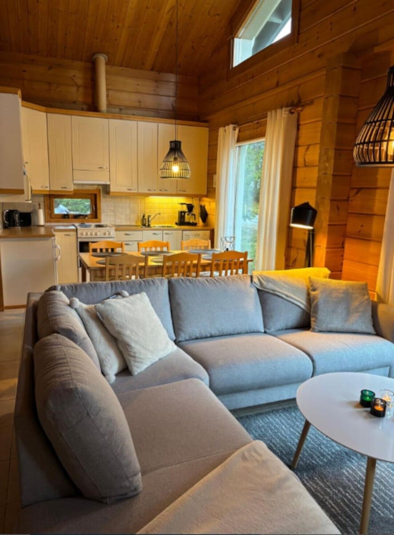 A modern log cabin interior with a sectional sofa, dining table, and kitchen area.