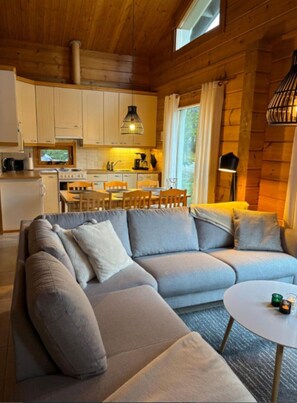 Ein modernes Blockhaushaus-Interieur mit einem Ecksofa, Esstisch und Küchenbereich.