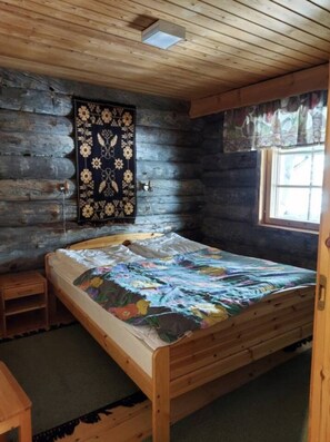 Ein Holzhütten-Zimmer mit Bett, einem kleinen Tisch, einem Fenster und Wandteppich.