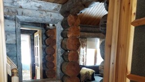 A log cabin interior with a staircase leading to a second level, a sofa in the living area, and a door frame. - Rukanjurmu 9 | Spacious 2BR Log Apt with Sauna (Ruka)