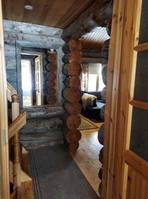 Ein Holzblockhaus-Innenraum mit einer Treppe, die zu einer zweiten Ebene führt, einem Sofa im Wohnbereich und einem Türrahmen.