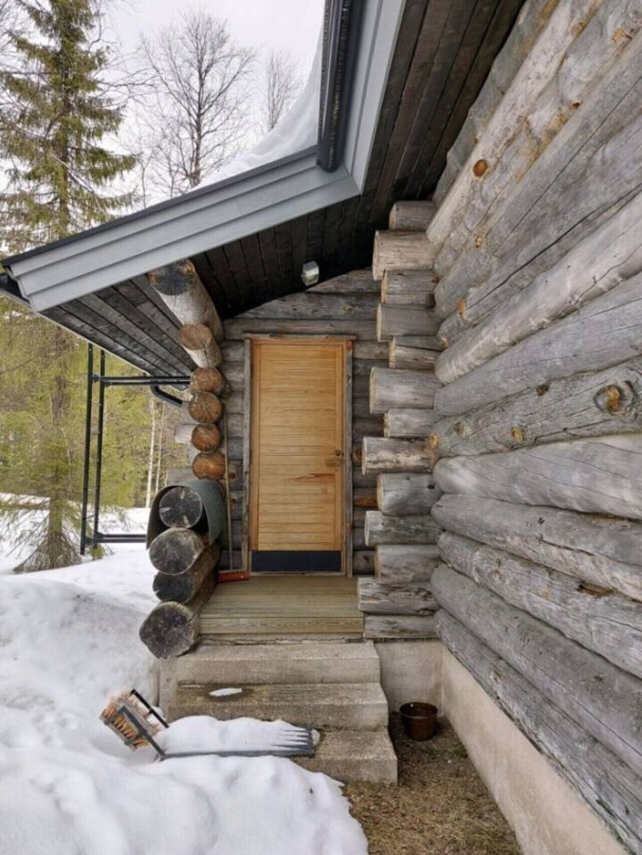 A log cabin with a wooden door, a porch with steps, and a snow-covered ground.