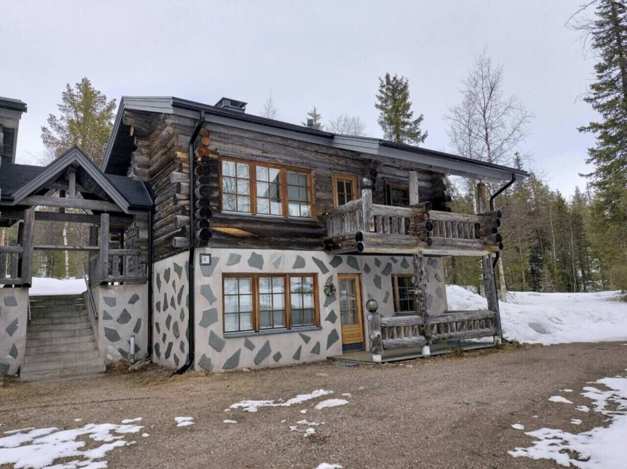 Eine Blockhütte mit Steinverkleidung, einem Balkon und einer Holzterrasse.