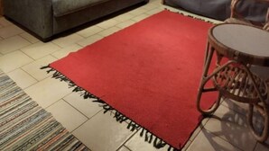 A room with a grey sofa, a red rug, a wooden ceiling, and a television on a stand. - Rukanjurmu 9 | Spacious 2BR Log Apt with Sauna (Ruka)
