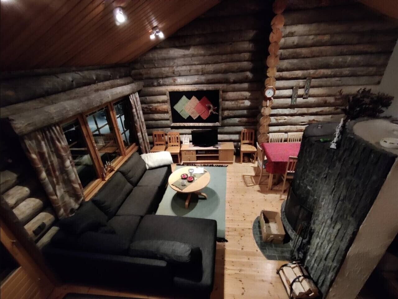 En stuga med träpanel på insidan, inredd med en soffa, ett soffbord och en öppen spis.