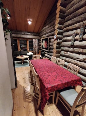 Ein rustikales Blockhaus-Interieur mit Esstisch, Stühlen, einer Uhr und einem gerahmten Bild an der Wand.