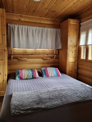 A wooden cabin room with a bed, a window with curtains, and a wooden cabinet. - Mäntyruka A2 | Cozy 1BR Cabin | Sauna & Fireplace (Ruka)