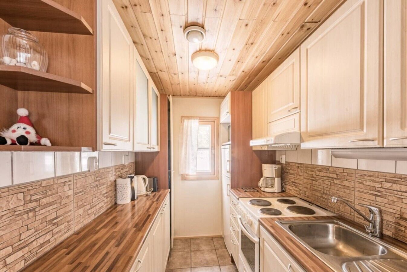 Une cuisine étroite avec des meubles de rangement en bois, une cuisinière, un évier et une fenêtre.