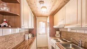 A narrow kitchen with wooden cabinets, a stove, a sink, and a window. - Mäntyruka A2 | Cozy 1BR Cabin | Sauna & Fireplace (Ruka)