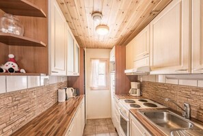 A narrow kitchen with wooden cabinets, a stove, a sink, and a window. - Mäntyruka A2 | Cozy 1BR Cabin | Sauna & Fireplace (Ruka)