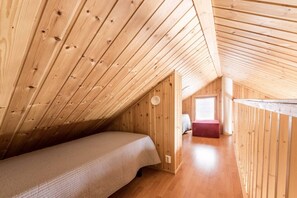 A small, wooden attic bedroom with a single bed, a window, and a door leading to another room. - Mäntyruka A2 | Cozy 1BR Cabin | Sauna & Fireplace (Ruka)