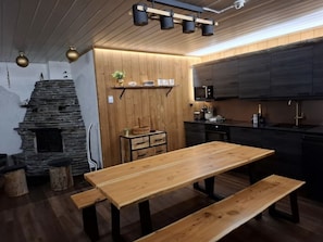 A cozy kitchen with a wooden table and bench, a stone fireplace, and modern cabinetry. - Rukapirtti | Spacious 5BR Chalet with Sauna (Ruka)