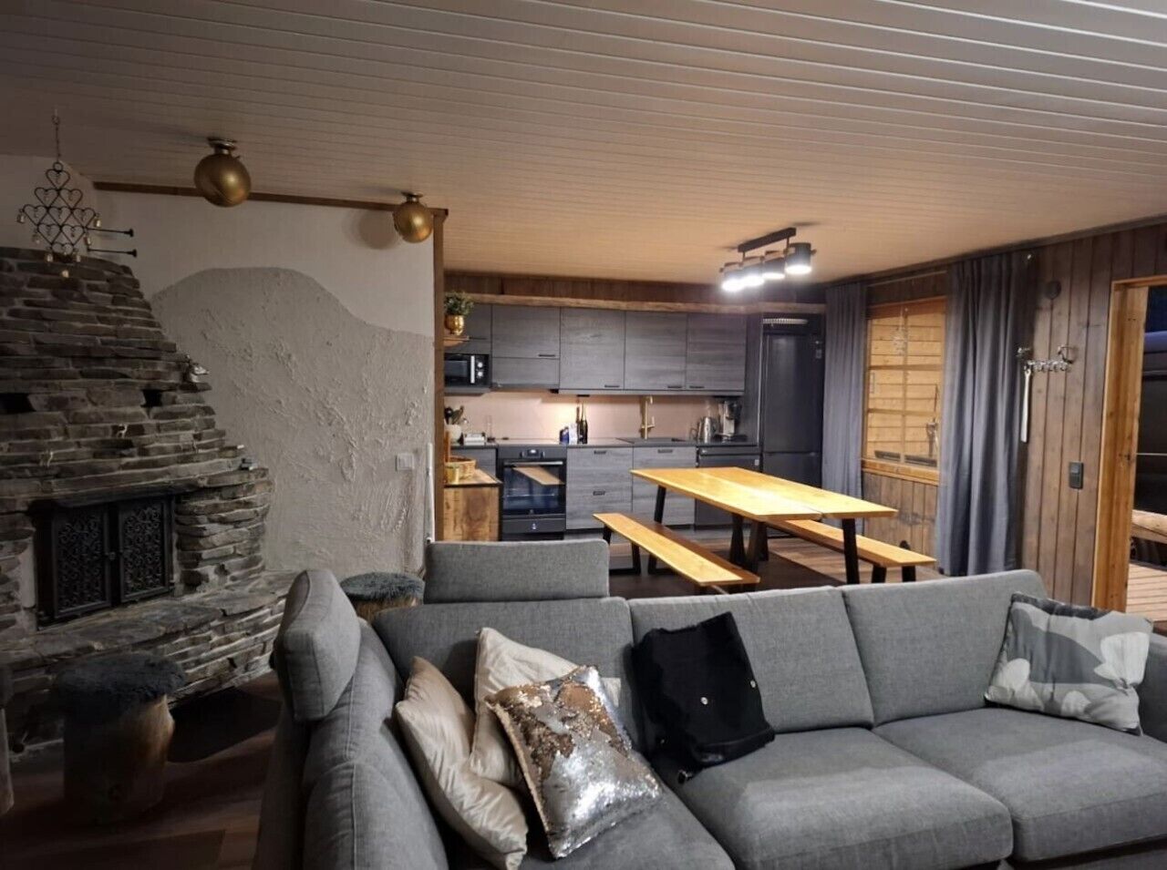 A modern living room with a stone fireplace, grey sofa, and a wooden dining table.
