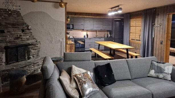 En moderne stue med en stenspejs, en grå sofa og et træspisebord.