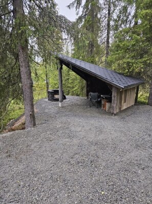 A covered outdoor area with a gravel ground, a wooden structure with a sloped roof, and a bench. - Rukapirtti | Spacious 5BR Chalet with Sauna (Ruka)
