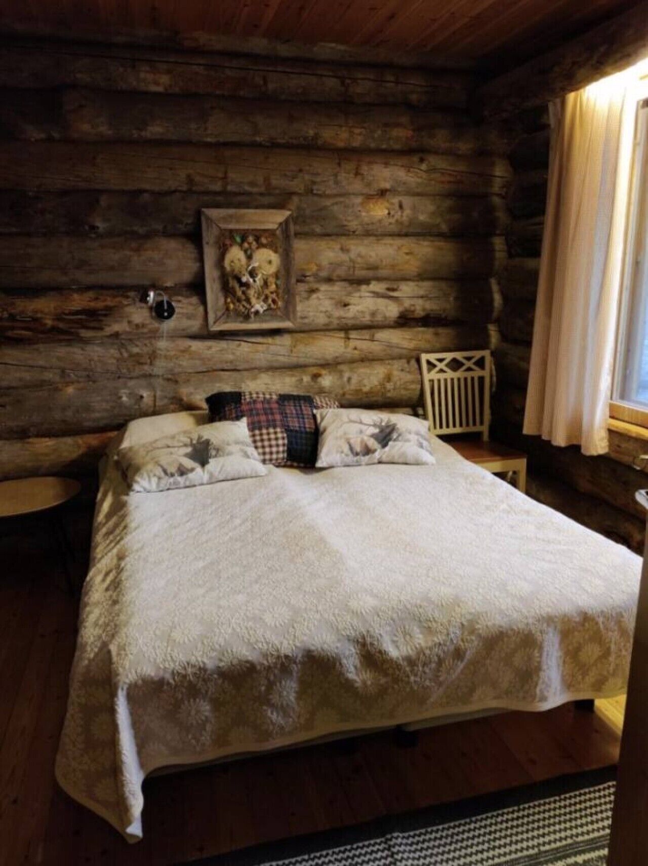 A log cabin room with a bed, a small table, and a wall-mounted picture.