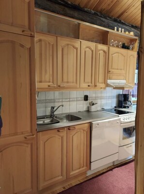 A kitchen with wooden cabinets, a stainless steel sink, a white dishwasher, and a stove. - Rukanjurmu 8 | Spacious 2BR Log Apt with Sauna (Ruka)